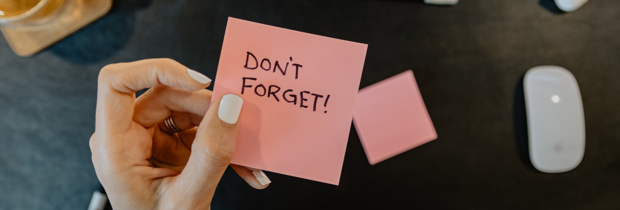 A woman holding a sticky note reminder that says "don't forget!"